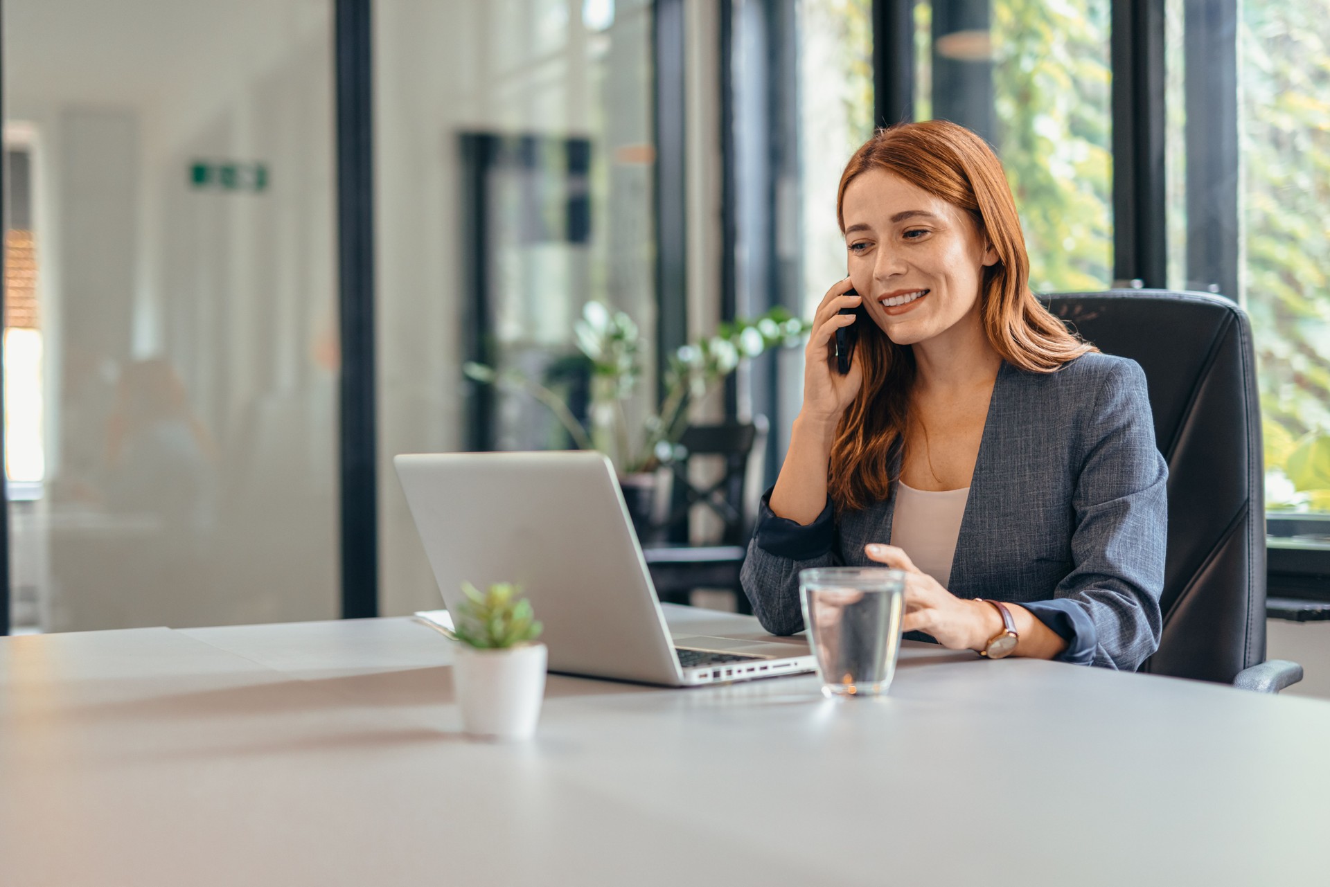 Businesswoman talking on phone in office, with laptop on desk.